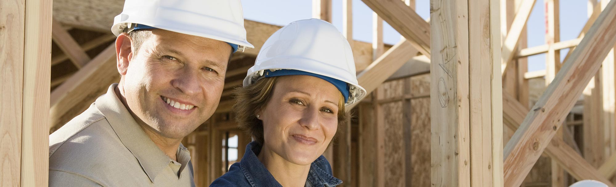Eine Frau und ein Mann mit Schutzhelmen stehen auf einer Baustelle.
